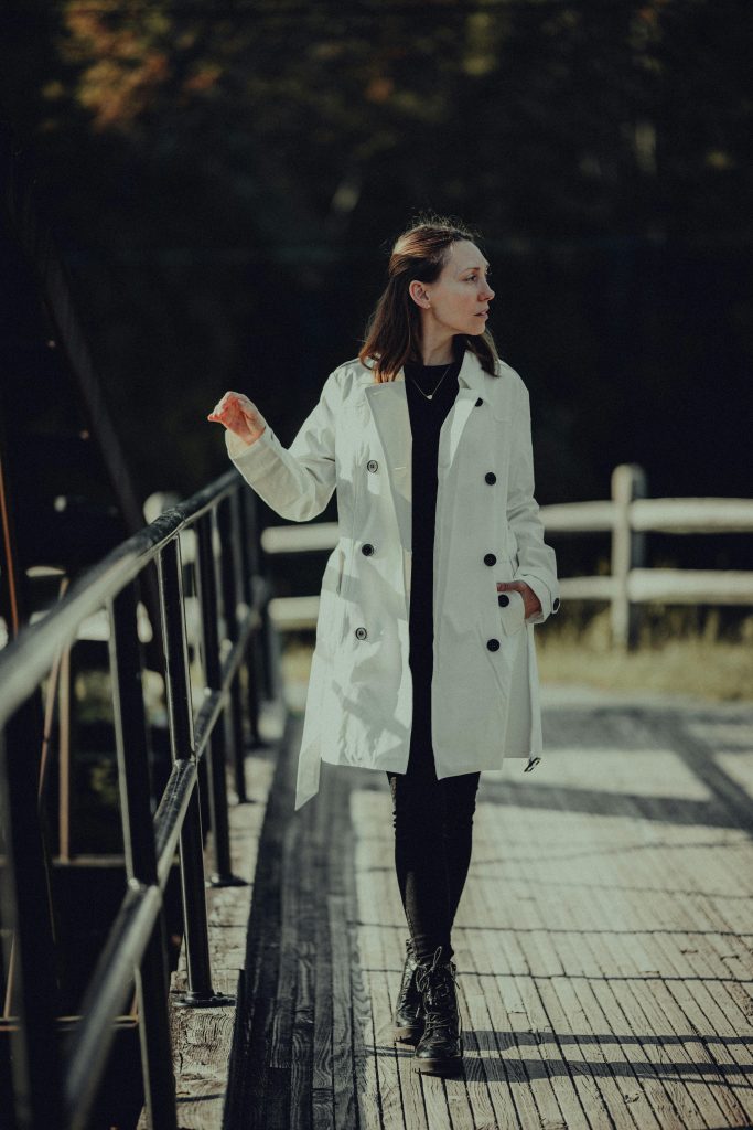 Frau in hellem Mantel geht nachdenklich über eine Holzbrücke im Sonnenlicht – Symbol für Balance zwischen Energie und Klarheit