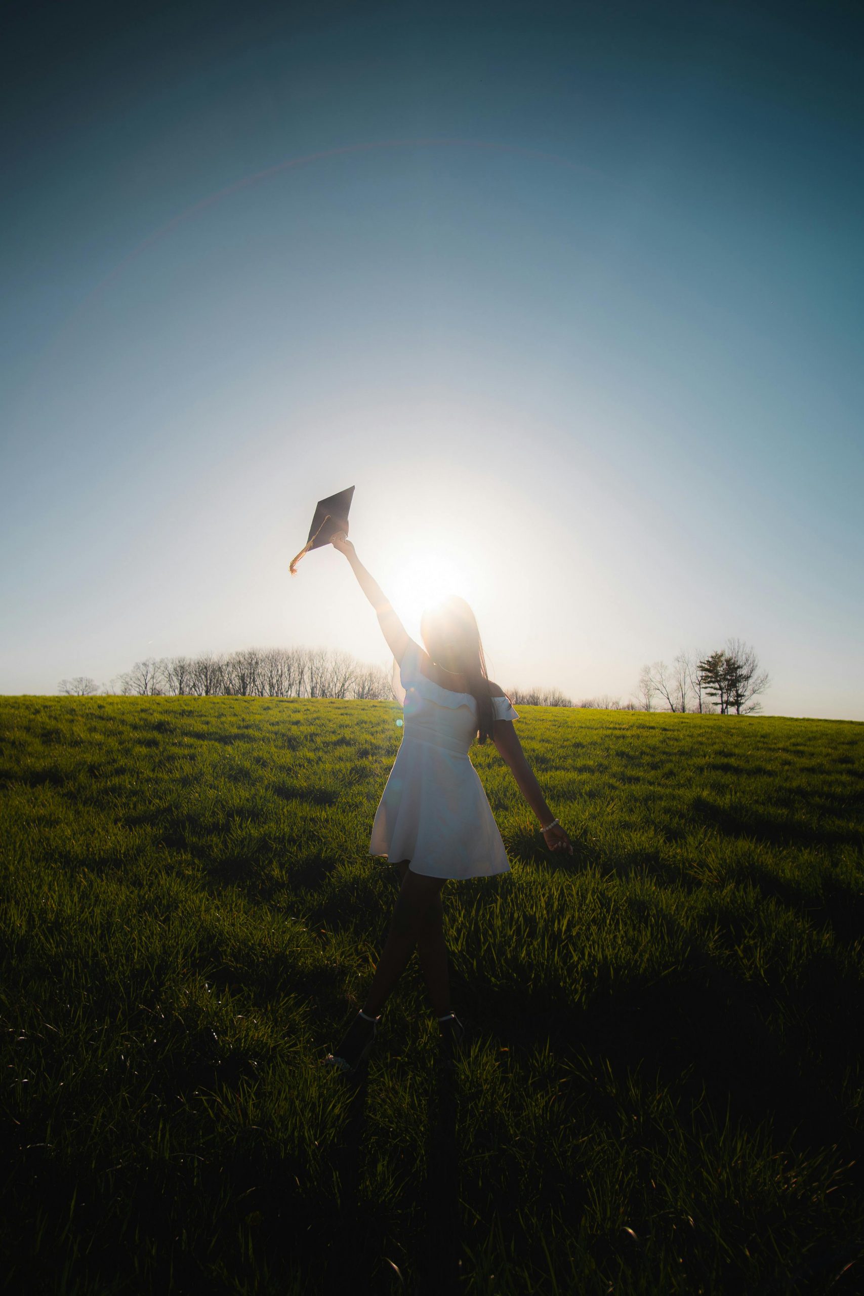 frau hält abschlusskappe auf einer wiese in den himmel als symbol für neuanfang, hoffnung und veränderung