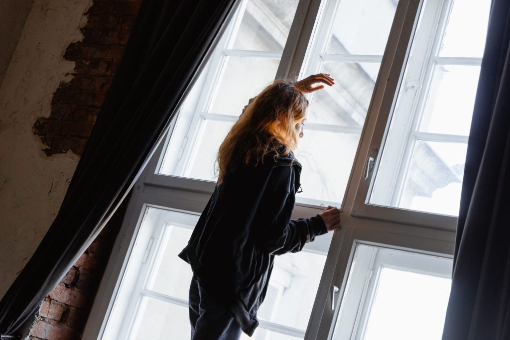 Nachdenkliche Frau am Fenster zwischen Hoffnung und Unsicherheit vor einer Partnerzusammenführung