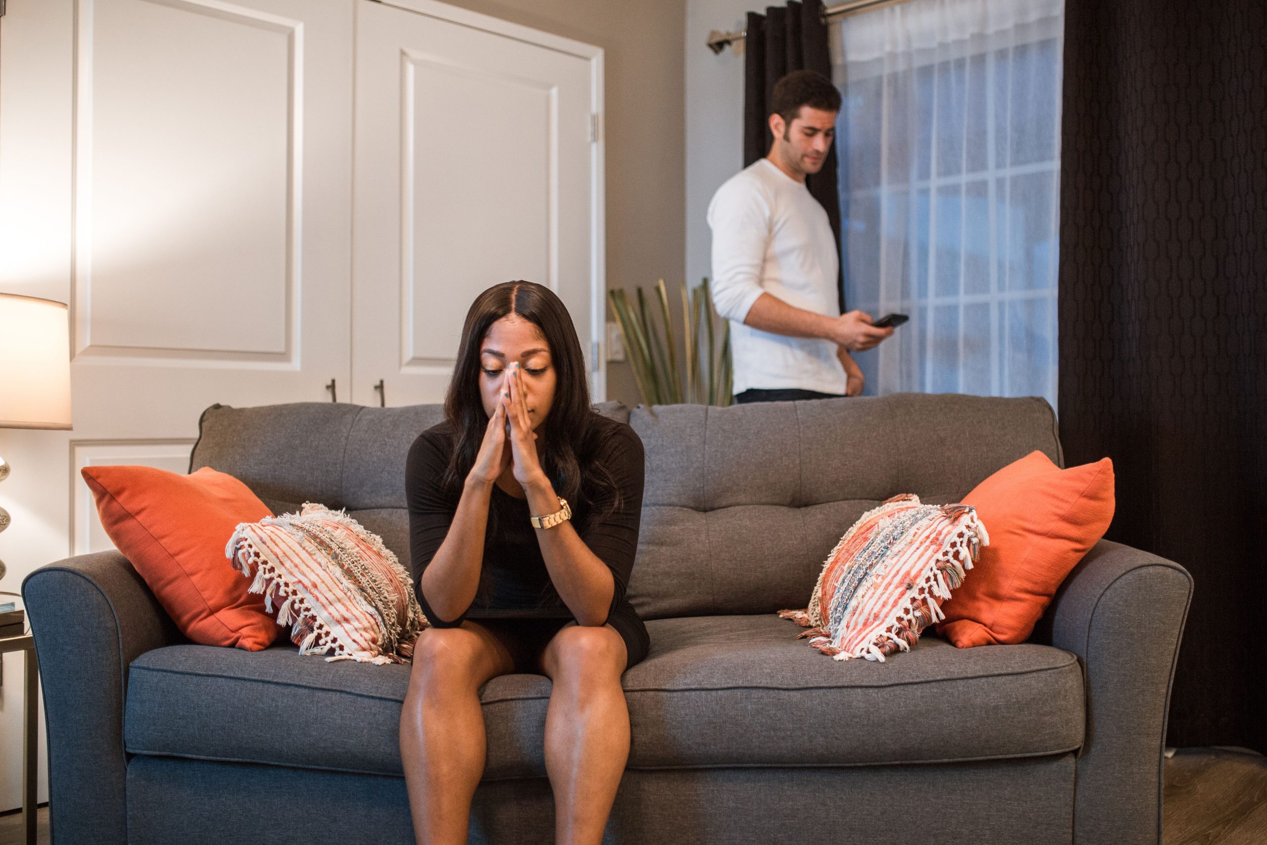 Frau sitzt auf einem Sofa, während ein Mann mit Abstand hinter ihr steht – Beziehungskonflikt und Distanz